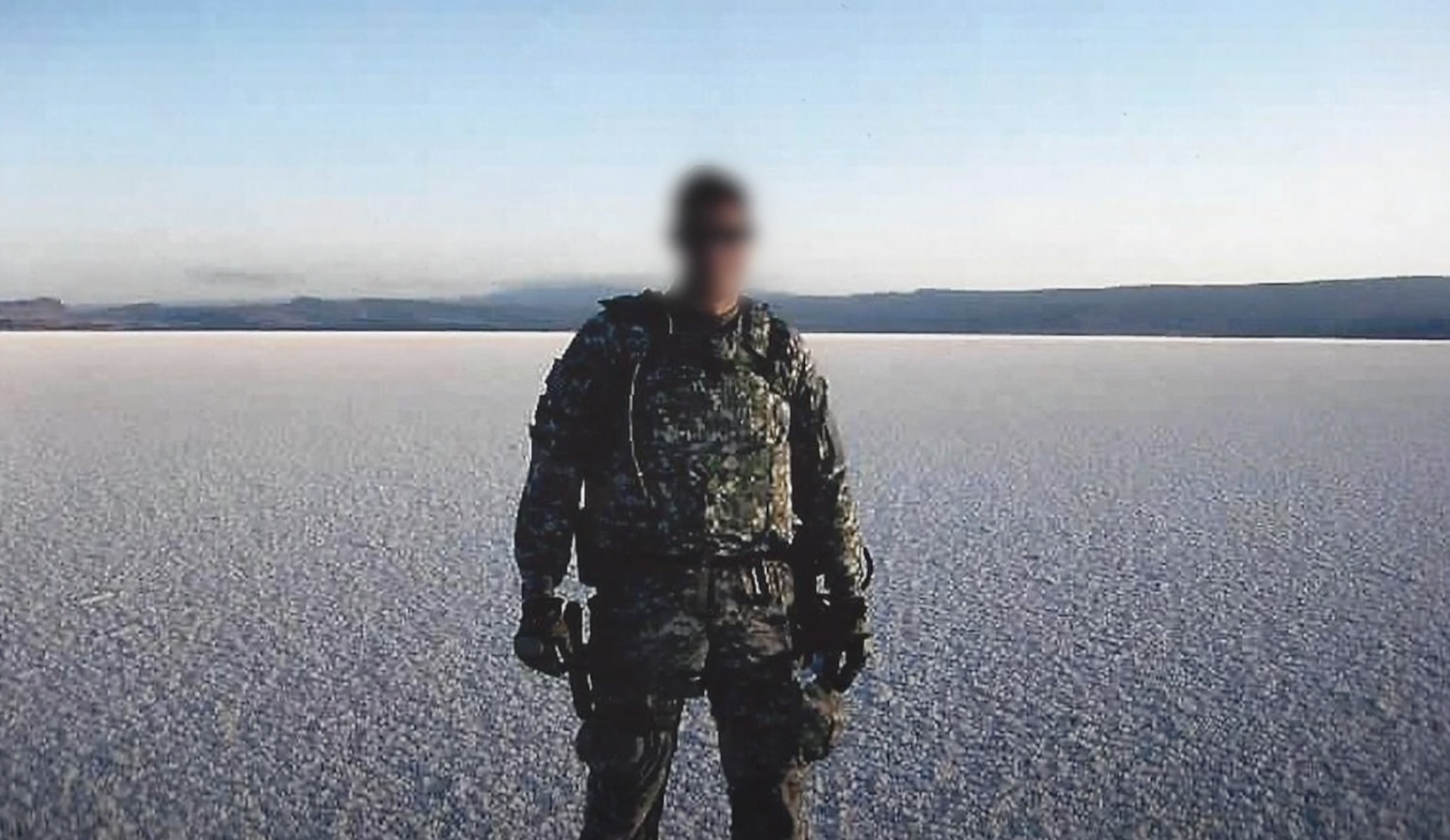 A man stands in U.S. military uniform in a desert scene.