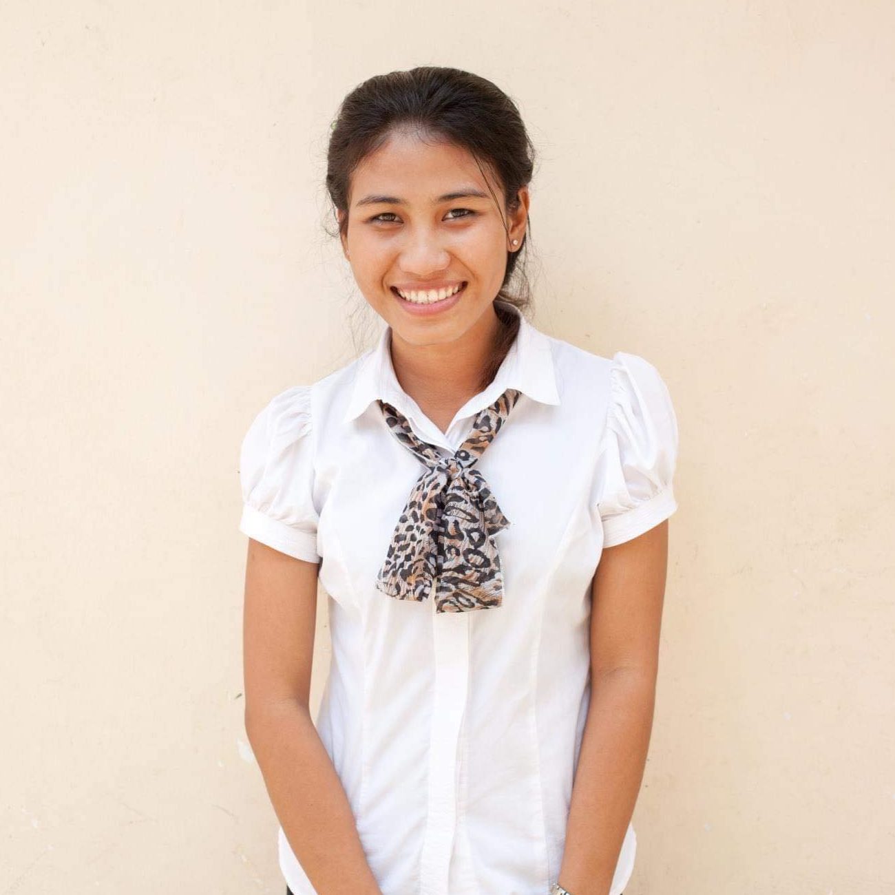 Sola, our Regional Aftercare Coordinator, stands smiling in front of a beige wall.