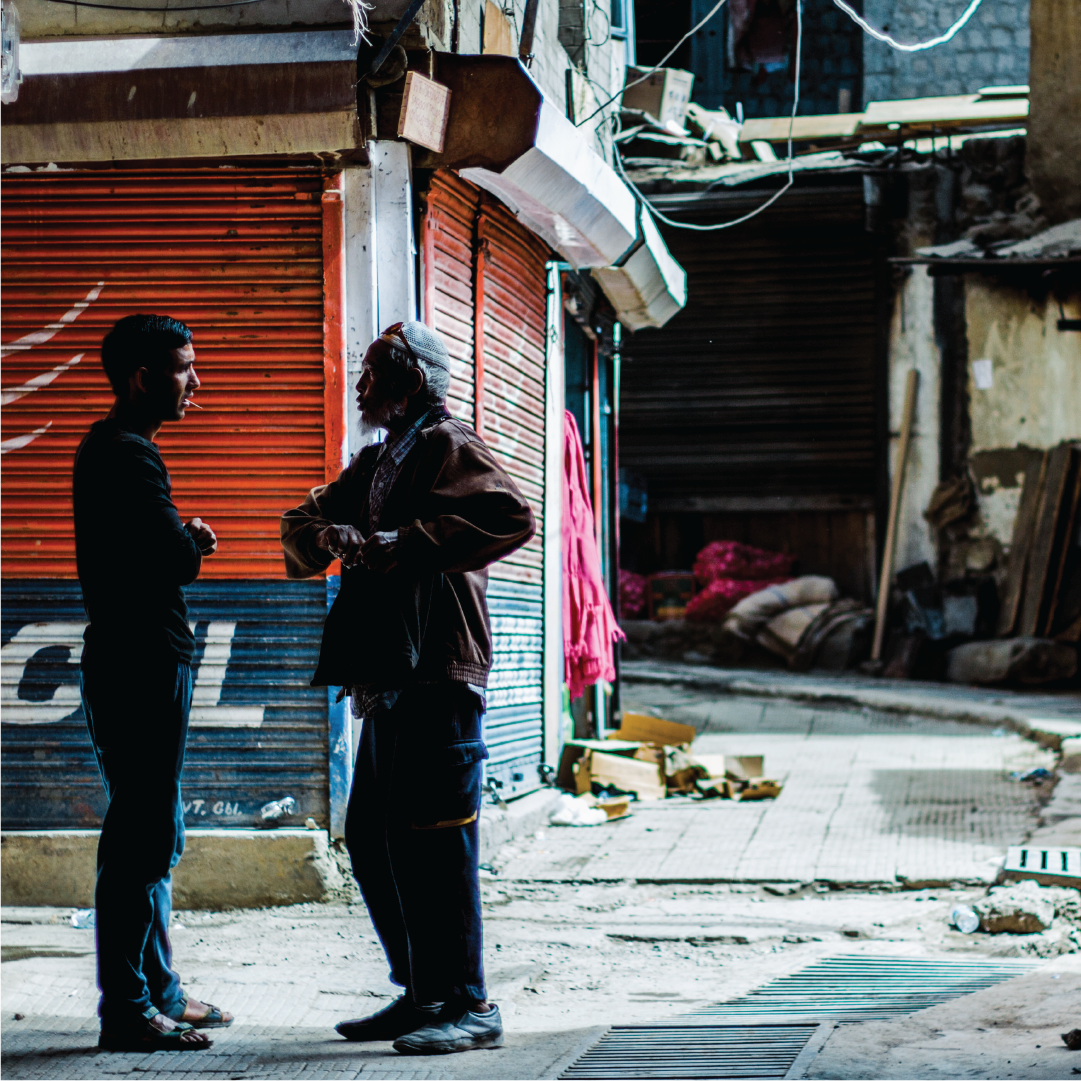 Representative image of national investigator speaking to man in a street alley in southeast Asia.