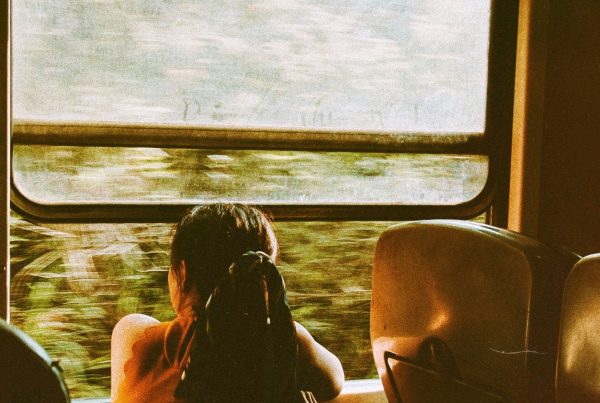 Young female Thai survivor sits looking out the window of a train.